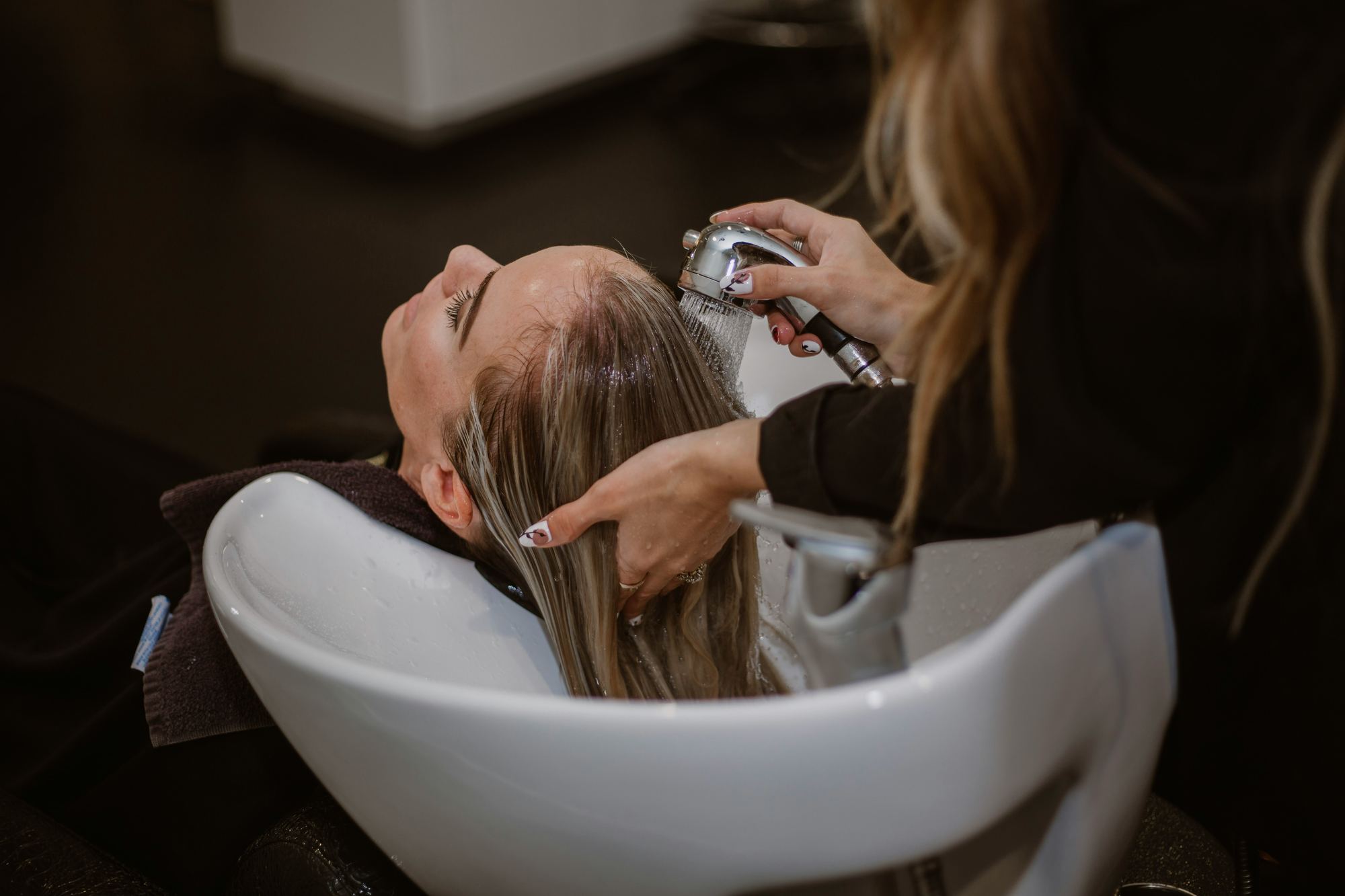 A stylist rinsing a client's hair at the shampoo basin